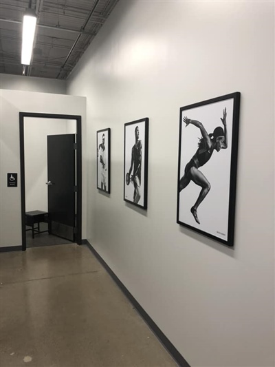 A hallway with white walls featuring black-and-white sports-themed photographs, leading to an open black door.