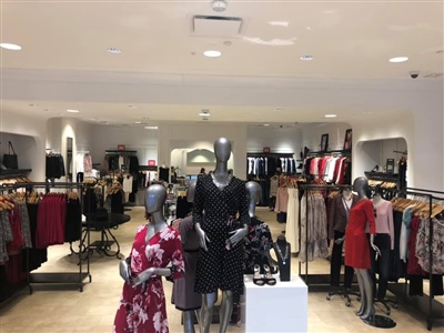 A retail store interior featuring mannequins dressed in stylish women's clothing, with racks of garments and accessories arranged neatly throughout the well-lit space.