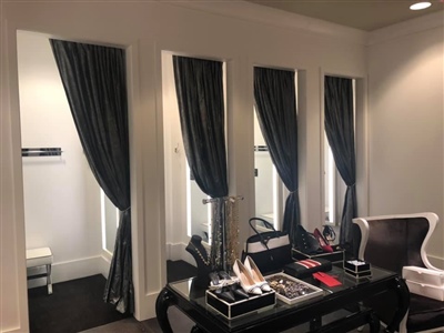 A stylish fitting room area with black curtains, a small seating area, and a table displaying accessories in a well-lit retail store.