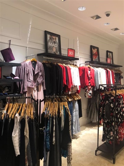 A retail store interior with clothing racks displaying a variety of women's apparel, framed promotional images on the wall, and well-lit surroundings.