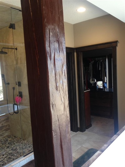 A hallway with a brown wrapped support column, leading to a bathroom with a glass shower enclosure and a closet.