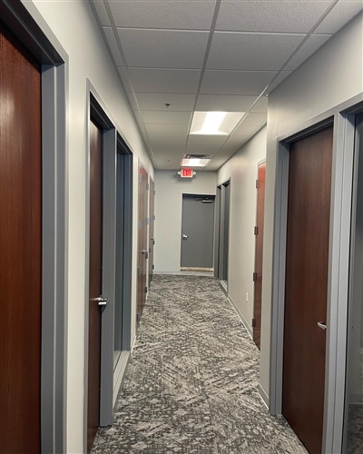 Office hallway with patterned carpet, white walls, and multiple wooden doors on both sides leading to various rooms.