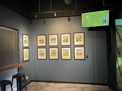 Indoor room with dark blue walls featuring a collection of framed pictures, a high table with stools, and a mounted TV displaying a sports game.