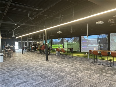 Large indoor space with patterned carpet, multiple seating areas, and large screens displaying virtual golf simulations.