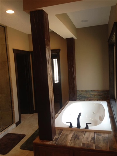 A bathroom with a large bathtub, beige walls, brown wrapped support columns, and a doorway leading to another room.