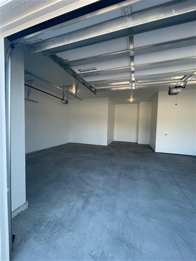 An empty garage with concrete flooring, white walls, and overhead lighting, featuring metal shelving units along the walls.