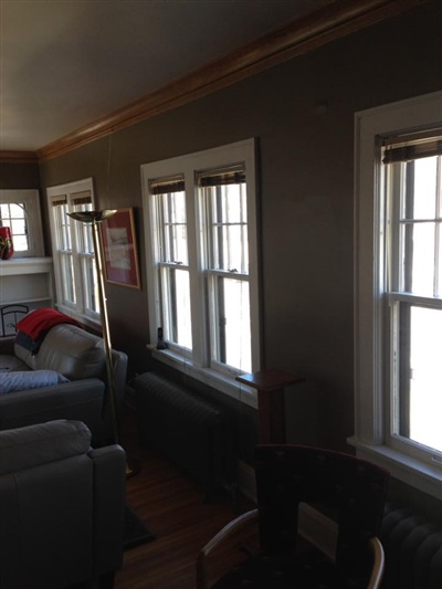 A living room with dark walls, multiple windows with blinds, gray sofas, a wooden floor, and a radiator.