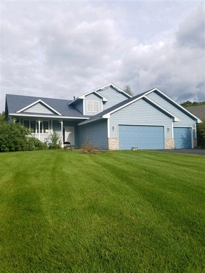 A light blue single-story house with a large garage, a well-manicured lawn, and a cloudy sky overhead.