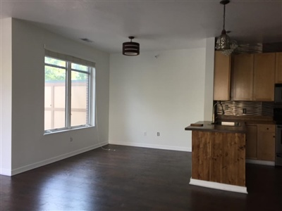 A modern kitchen with wooden cabinets, stainless steel appliances, dark hardwood floors, and an adjacent dining area with a large window.