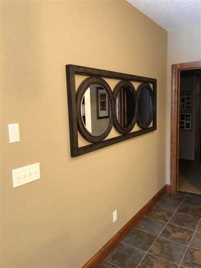 A hallway with beige walls, a decorative mirror with three circular sections, tiled flooring, and a wooden doorframe leading to another room.