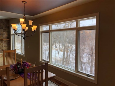 A dining room with large windows offering a view of a snowy landscape, a wooden dining table and chairs, and a chandelier hanging from the ceiling.