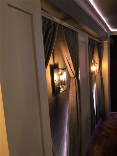 Wall with elegant sconces and draped curtains, illuminated by soft, ambient lighting in a cozy home theater setting.