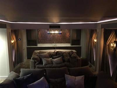 Home theater room with plush gray sofas, decorative wall sconces, and ambient lighting, creating a cozy and inviting atmosphere.