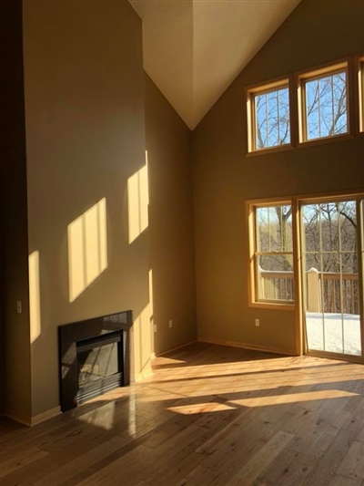 Bright room with high vaulted ceilings, large windows, a fireplace, and a sliding glass door opening to a snowy outdoor view.