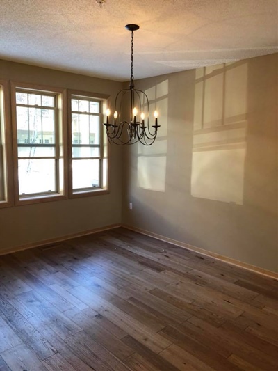 Empty room with wooden flooring, a chandelier, and three large windows letting in natural light.