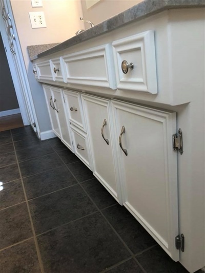 White bathroom vanity with multiple drawers and cabinets, gray countertop, and dark tiled floor.