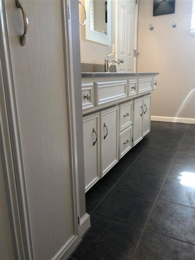 Bathroom with a white double-sink vanity, gray countertop, multiple drawers and cabinets, and dark tiled floor.