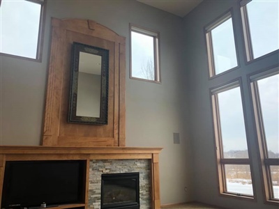 Living room with a high ceiling, large windows, a stone fireplace, and a wooden mantle with a mirror above it.