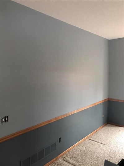 A room with light blue walls, a darker blue wainscoting, wooden trim, and beige carpet.