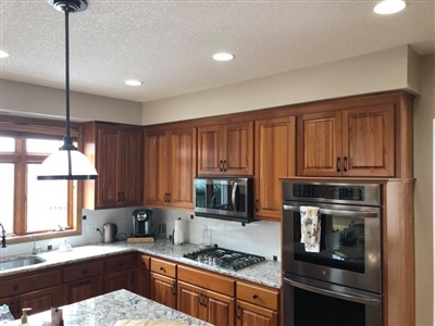 A kitchen with wooden cabinets, stainless steel appliances, a granite countertop, and a pendant light above the island.